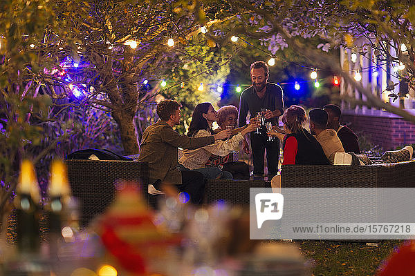 Freunde trinken unter Bäumen mit Lichterketten bei einer Gartenparty