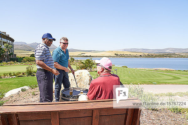 Männliche Golffreunde unterhalten sich beim Biertrinken auf einer sonnigen Golfplatzterrasse