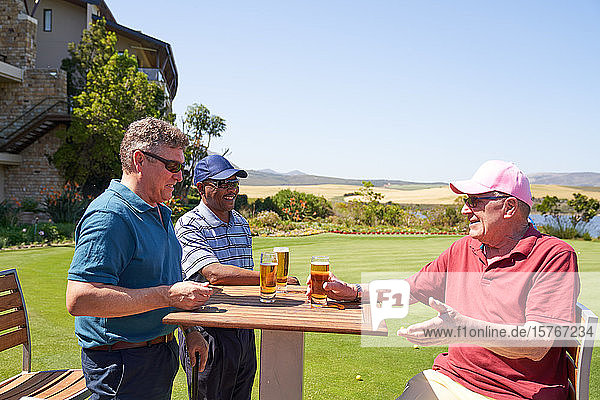 Glückliche reife männliche Golfer trinken Bier im sonnigen Clubhaus des Golfplatzes