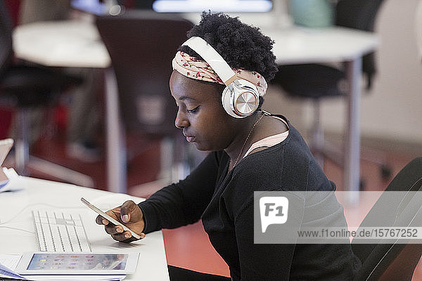 Schülerin mit Kopfhörern und Smartphone im Klassenzimmer
