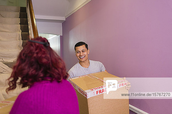 Ein glückliches Paar zieht in ein neues Haus und trägt Kartons die Treppe hinauf.