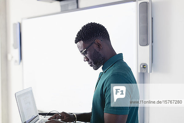 Männlicher Professor mit Laptop neben der Projektionsfläche im Klassenzimmer