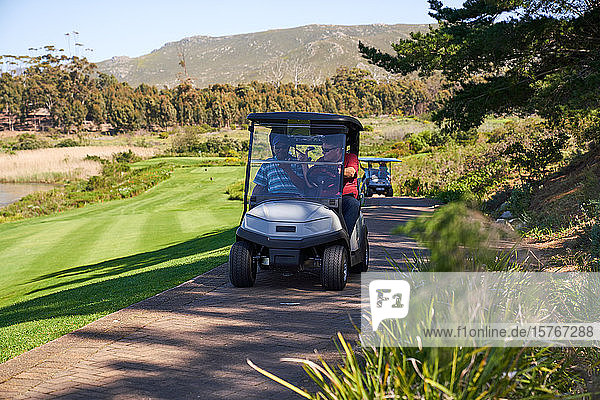 Männliche Golfer fahren im Golfwagen auf einem sonnigen Golfplatzweg