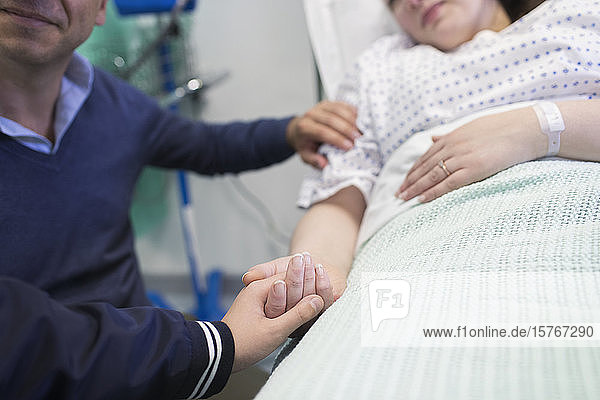 Zärtlicher Sohn hält die Hände seiner Mutter  die im Krankenhausbett ruht