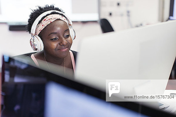 Lächelnde Studentin einer Volkshochschule mit Kopfhörern am Computer im Klassenzimmer