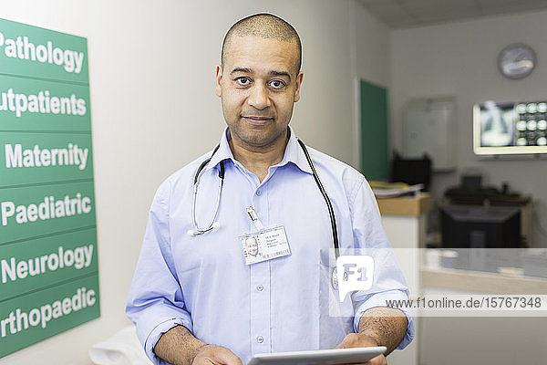 Porträt selbstbewusster männlicher Arzt mit digitalem Tablet in einem Krankenhauskorridor