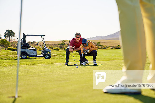 Männliche Golfer planen den Putt auf sonnigen Golfplätzen