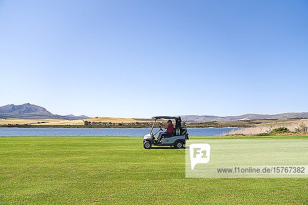 Männlicher Golfer fährt mit seinem Golfwagen am See entlang auf einem sonnigen Golfplatz