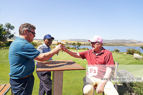 Ältere männliche Golfer trinken Bier auf der sonnigen Terrasse eines Golfclubs
