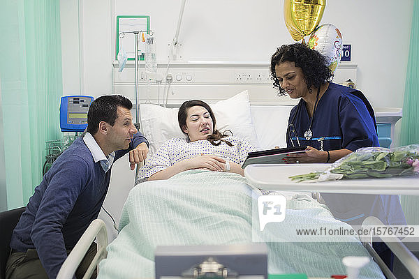 Arzt mit digitalem Tablet bei der Visite  Gespräch mit Paar im Krankenhauszimmer