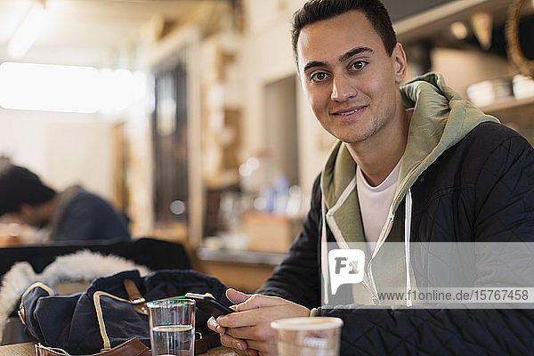 Portrait confident young male college student using smart phone in cafe