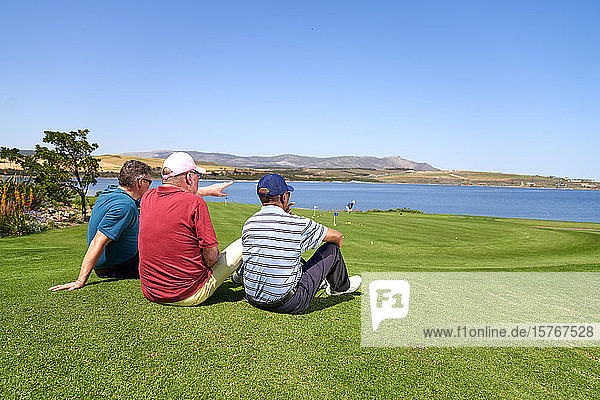 Männliche Golfer beim Entspannen mit Blick auf den See vom sonnigen Golfplatz aus