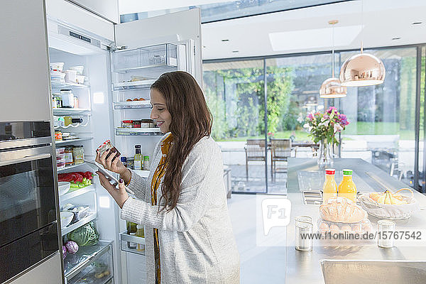 Frau mit digitalem Tablet am Kühlschrank in der Küche