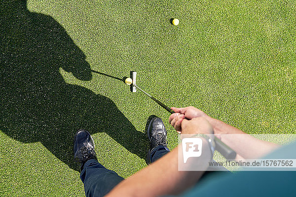Standpunkt eines Mannes  der einen Golfball auf ein sonniges Grün legt