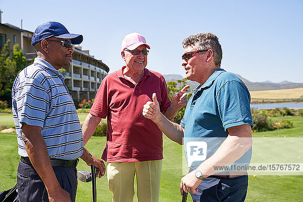 Glückliche männliche Golffreunde unterhalten sich auf einem sonnigen Golfplatz