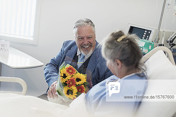 Glücklicher älterer Mann mit Blumenstrauß  der seine Frau im Krankenhaus besucht
