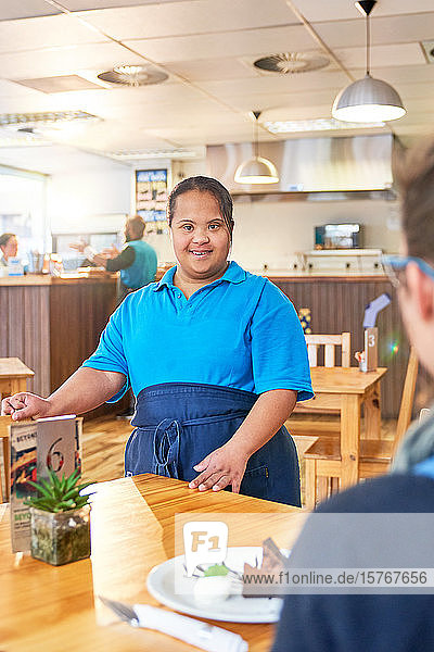 Porträt einer selbstbewussten jungen Kellnerin mit Down-Syndrom in einem Cafe