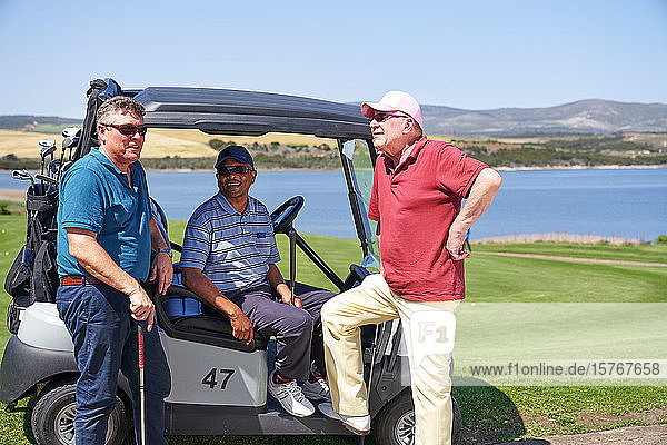 Glückliche reife männliche Golfer unterhalten sich am sonnigen Golfwagen