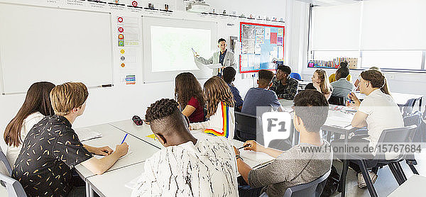 Gymnasiasten beobachten den Lehrer auf der Projektionsfläche während des Unterrichts im Klassenzimmer