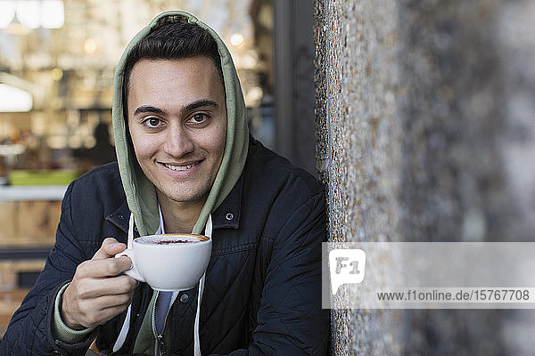 Porträt eines lächelnden  selbstbewussten jungen Mannes  der in einem Straßencafé Kaffee trinkt