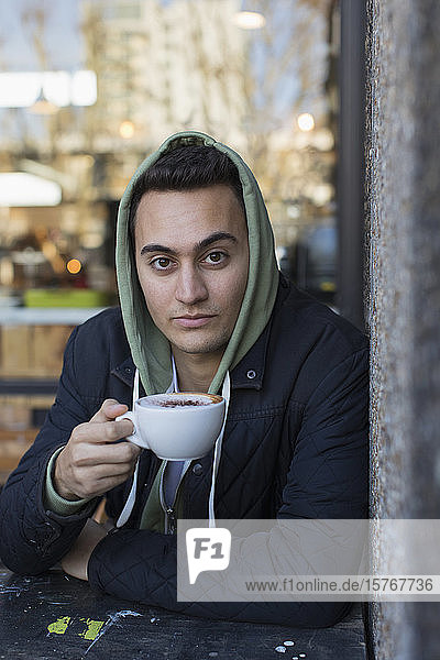 Porträt selbstbewusster junger Mann in Kapuzenjacke trinkt Cappuccino