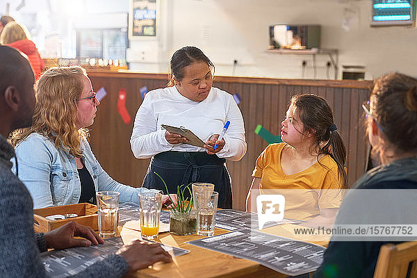 Junge Kellnerin mit Down-Syndrom nimmt in einem Café eine Bestellung auf