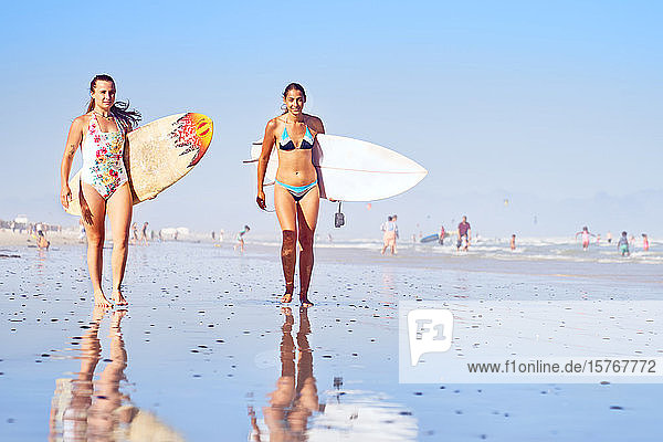 Portrait confident young female surfers on sunny ocean beach