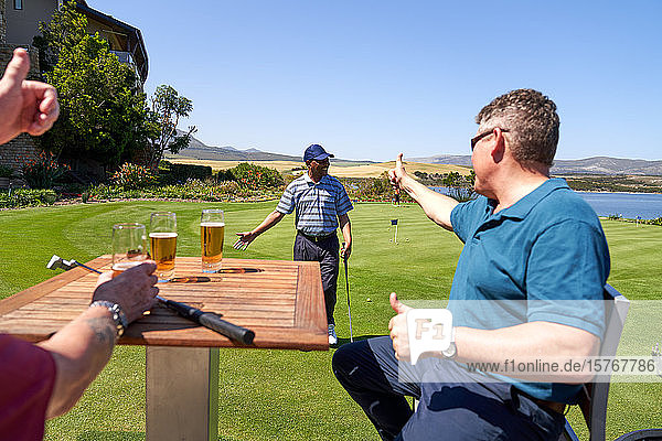 Männliche Golfer trinken Bier und feuern ihre Freunde auf dem Übungsgrün an.