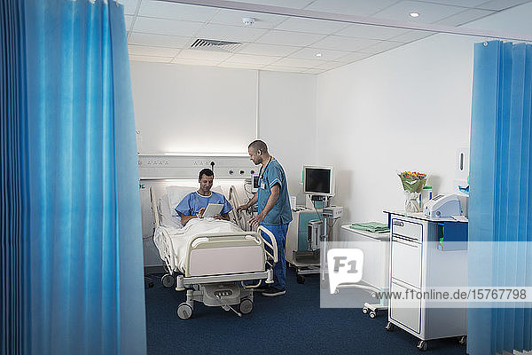 Male nurse talking with patient using digital tablet in hospital bed