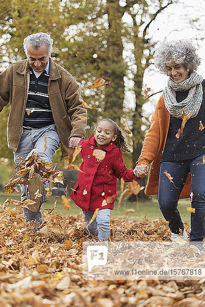 Playful grandparents and granddaughter kicking autumn leaves in park