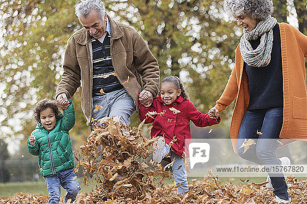 Verspielte Großeltern und Enkelkinder beim Kicken von Herbstblättern im Park