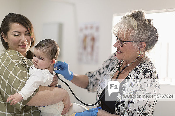 Female pediatrician with stethoscope examining baby girl in examination room