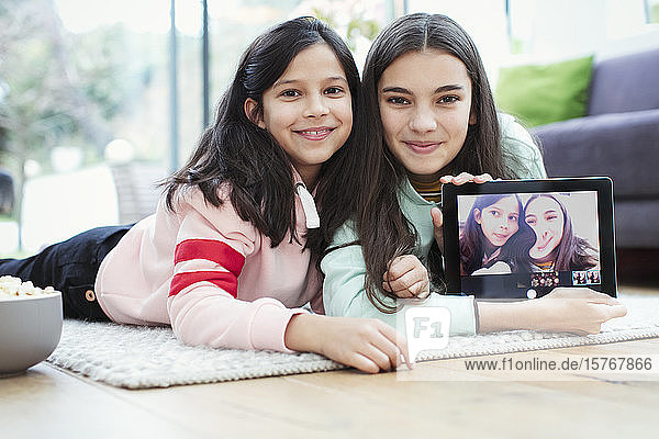 Porträt lächelnder Schwestern mit digitaler Tablet-Kamera auf dem Boden des Wohnzimmers
