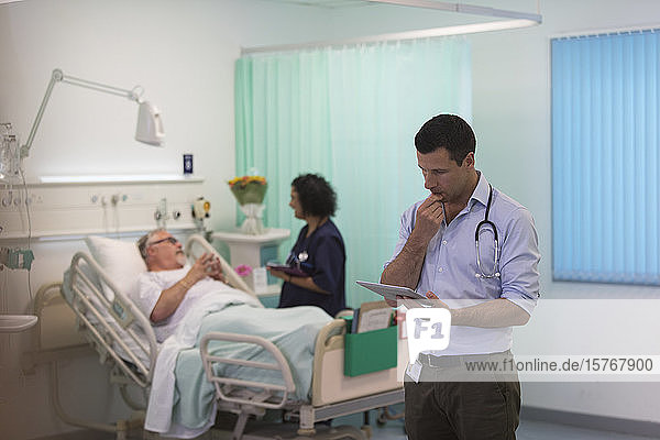 Männlicher Arzt mit digitalem Tablet bei der Visite im Krankenhauszimmer