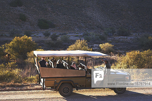 Safari-Guide und Gruppe im Geländewagen auf sonniger Schotterpiste