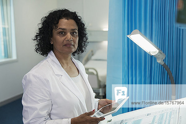 Porträt einer selbstbewussten  entschlossenen Ärztin  die ein digitales Tablet in einem Krankenhauszimmer benutzt