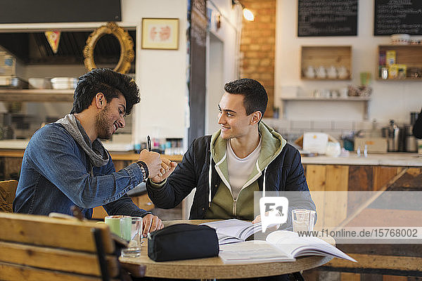 Junge männliche Studenten  die in einem Café lernen und sich die Hände reichen