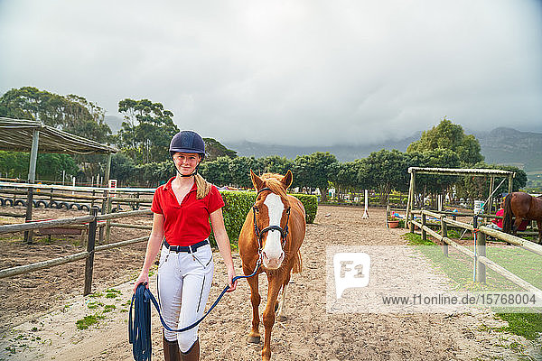 Porträt selbstbewusstes Teenager-Mädchen  das ein Pferd über eine ländliche Koppel führt