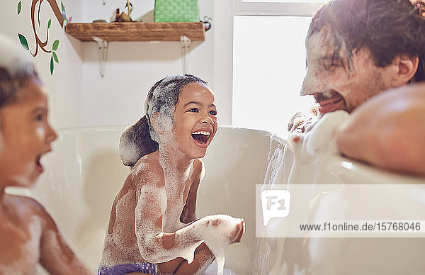 Playful daughters in bathtub wiping bubbles on fatherâ€™s face