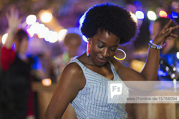 Unbeschwerte Frau mit Neon-Ohrringen tanzt auf einer Party