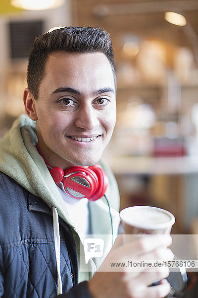 Porträt eines lächelnden  selbstbewussten jungen Mannes  der in einem Café Kaffee trinkt