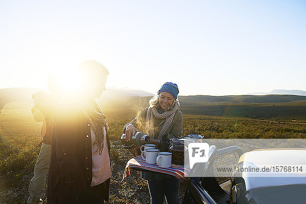 Glückliche ältere Frau auf Safari schenkt bei Sonnenaufgang Tee für einen Freund ein