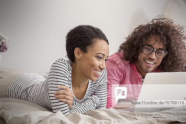 Lächelndes Paar mit Laptop auf dem Bett