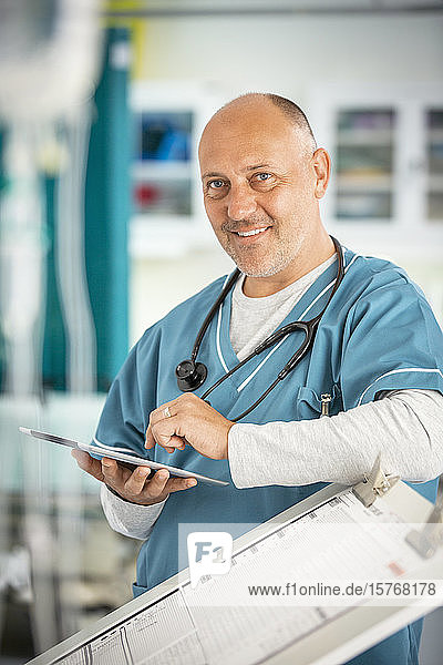 Porträt eines lächelnden  selbstbewussten männlichen Arztes  der ein digitales Tablet im Krankenhaus benutzt