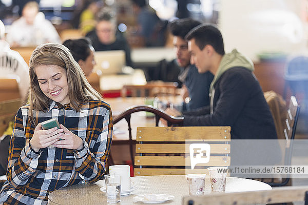 Lächelnde junge Frau mit Smartphone in einem Café