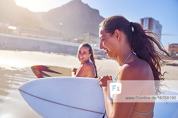 Glückliche junge Freundinnen mit Surfbrettern am sonnigen Strand