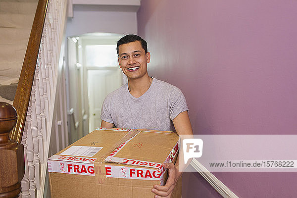 Porträt eines glücklichen Mannes  der einen Umzugskarton im Korridor trägt