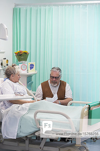 Älterer Mann mit Grußkarte  der seine im Krankenhaus liegende Frau besucht
