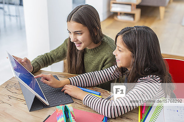 Mädchen machen Hausaufgaben und teilen sich ein digitales Tablet am Tisch