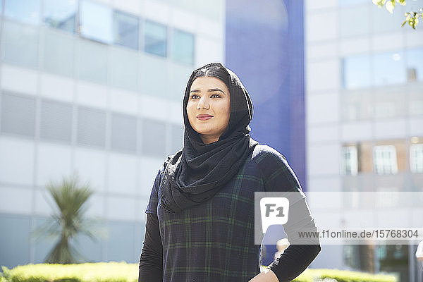 Porträt selbstbewusste junge Frau mit Hidschab vor einem sonnigen Gebäude
